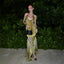 Woman in a yellow and black patterned dress standing against a green leafy background